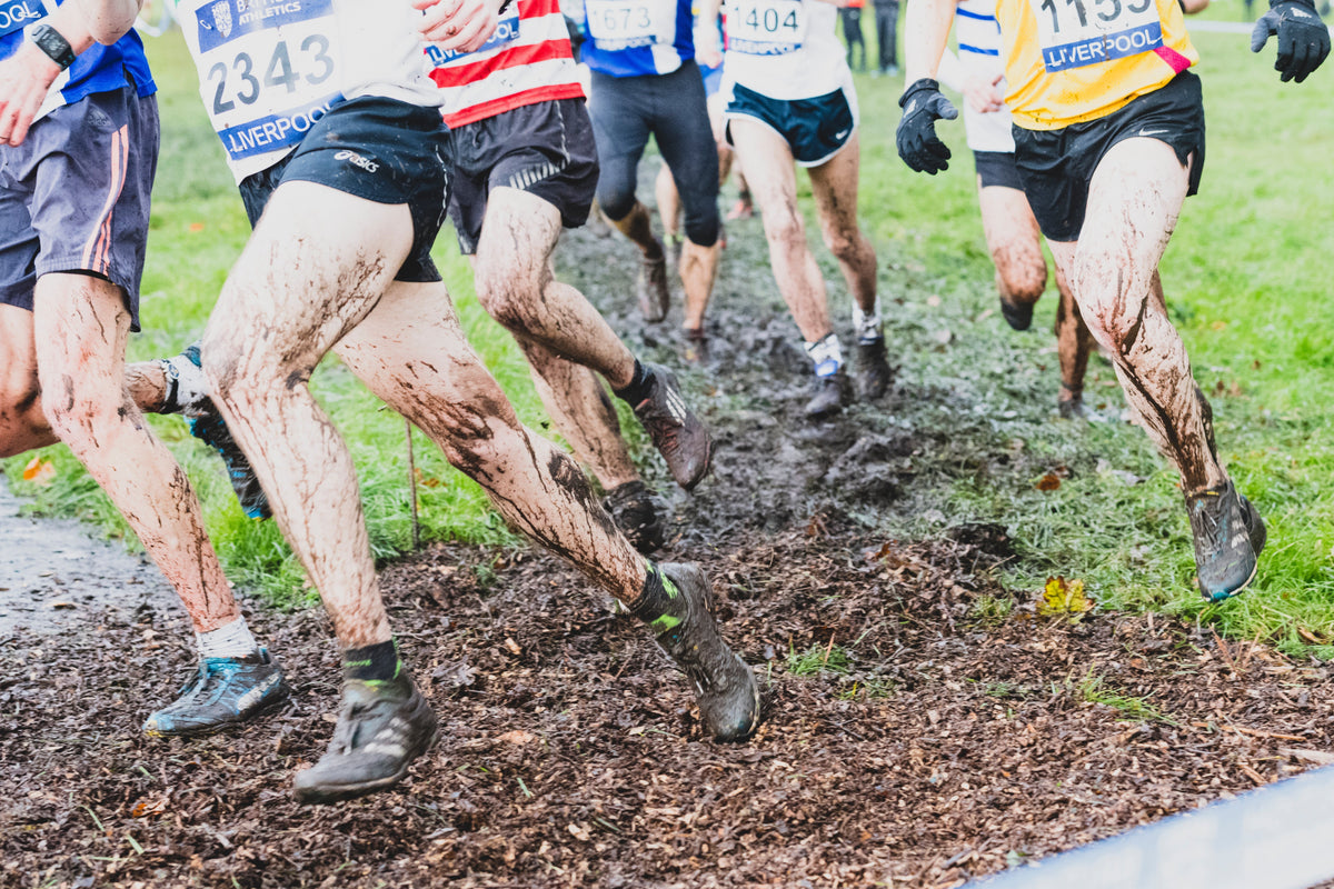 xc spikes v trail shoes in 2026 image shows men competing in cross country spikes in thick mud